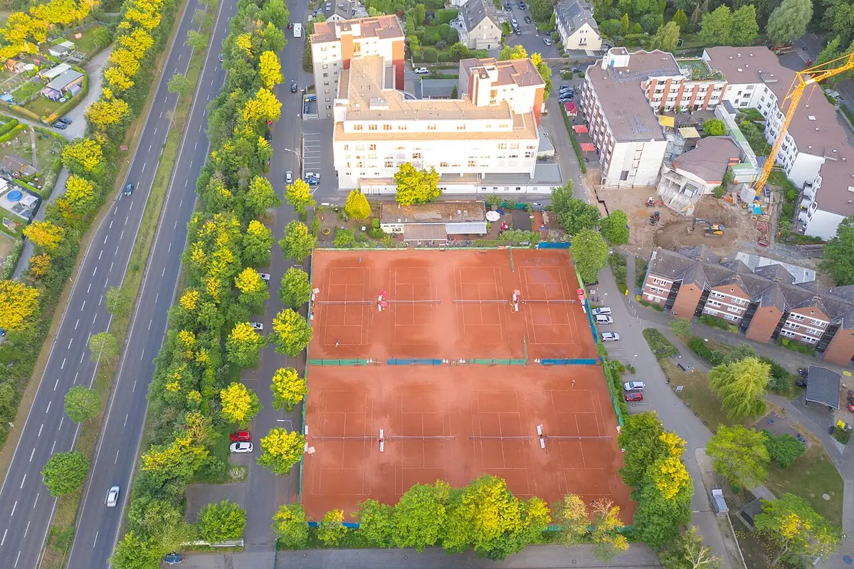 Cụm hai sân tennis đất nện nhìn từ trên cao giữa hàng cây và khu dân cư