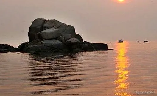Cụm đá giữa biển lúc hoàng hôn, mặt trời phản chiếu vệt vàng trên mặt nước