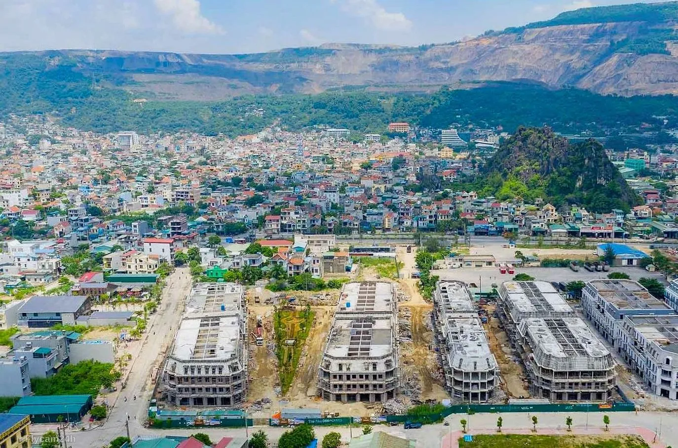 Dãy nhà phố liền kề đang thi công phần thô giữa thị trấn, phía sau là núi và khu dân cư, nhìn chéo từ flycam