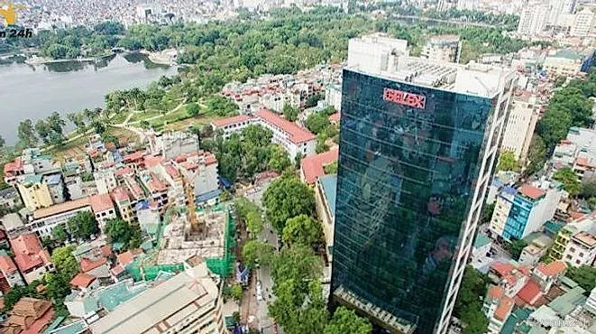 Tòa nhà văn phòng mặt kính cao tầng giữa khu phố thấp tầng Hà Nội, phía sau là hồ nước và cây xanh, nhìn chéo từ flycam
