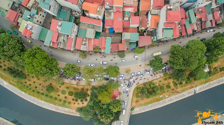 Ảnh flycam nhìn thẳng xuống một đoạn phố cong chạy dọc bờ kênh, hai bên là dãy nhà mái đỏ và hàng cây