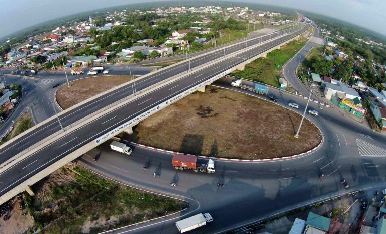 Nút giao cao tốc với cầu vượt và đường vòng, xe tải lưu thông, khu dân cư hai bên nhìn từ trên cao